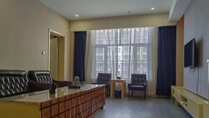 Una sala de estar moderna con sofá, sillones, una mesa de centro, televisor y ventanas amplias con cortinas.