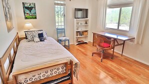 Un dormitorio con cama, escritorio, silla, televisor y ventana.