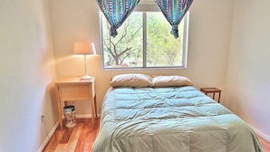 A bedroom with a bed, a nightstand, a lamp, and a window with curtains. - Happy Trails Hideaway (Tucson)