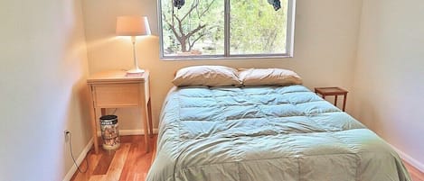 Un dormitorio con cama, mesita de noche, lámpara y ventana con cortinas.