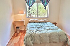 A bedroom with a bed, a nightstand, a lamp, and a window with curtains. - Happy Trails Hideaway (Tucson)
