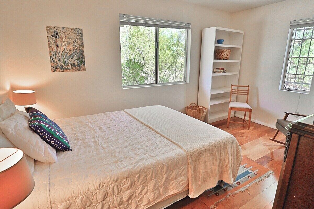 Ein Schlafzimmer mit Bett, Nachttisch, Lampe, Fenster, Bücherregal und Stuhl.