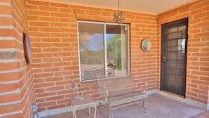 A brick building with a metal bench and table outside, a door, and a window with a view. - Happy Trails Hideaway (Tucson)