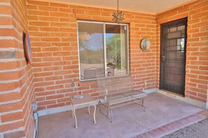 A brick building with a metal bench and table outside, a door, and a window with a view. - Happy Trails Hideaway (Tucson)