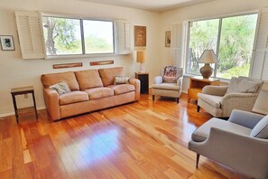 A living room with a wooden floor, a beige sofa, a grey armchair, and a small table with a lamp. - Happy Trails Hideaway (Tucson)