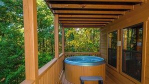 A wooden deck with a hot tub, wooden railings, and a view of a forest. - 3 BR/3 bath (sleeps 8) located between GBurg & PF! Hot tub, pool table, privacy! (Sevierville)