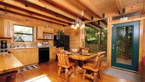 A wooden cabin interior with a kitchen, dining area, and a door leading outside. - 3 BR/3 bath (sleeps 8) located between GBurg & PF! Hot tub, pool table, privacy! (Sevierville)