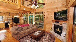 A cozy cabin interior with a wooden interior, a fireplace, a television mounted on the wall, and a dining area with a table and chairs. - 3 BR/3 bath (sleeps 8) located between GBurg & PF! Hot tub, pool table, privacy! (Sevierville)