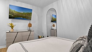 Ein Schlafzimmer mit Bett, Kommode, Spiegel, Fernseher und einem Bild von einem See.