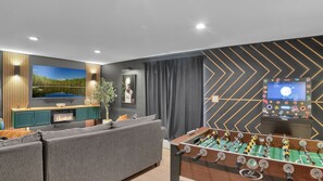 A modern living room with a foosball table, a flat-screen TV, and a fireplace.