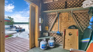 A wooden cabin with a dock, propane tanks, and a smiley face sign.