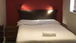 A single bed with white bedding, a dark headboard, and a red accent wall. - The Bull and Bush Hotel Kingston (Kingston Upon Thames)