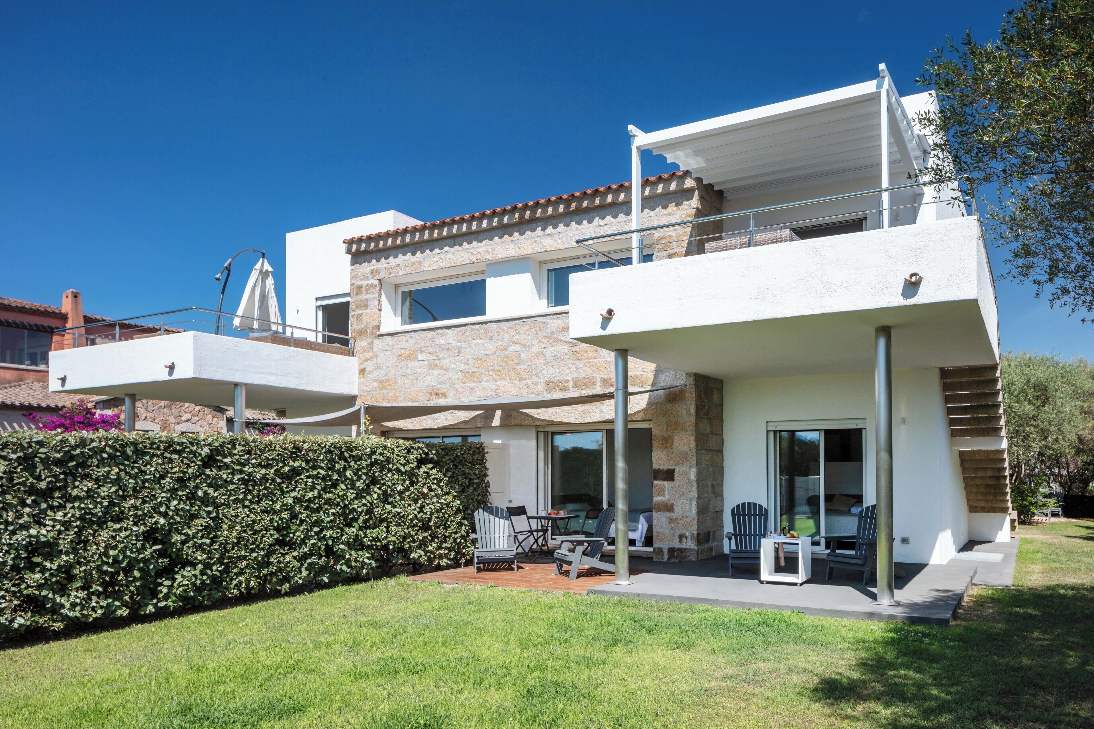 Une maison moderne à deux étages dotée d’un patio, d’un espace salon extérieur et d’une façade en pierre.