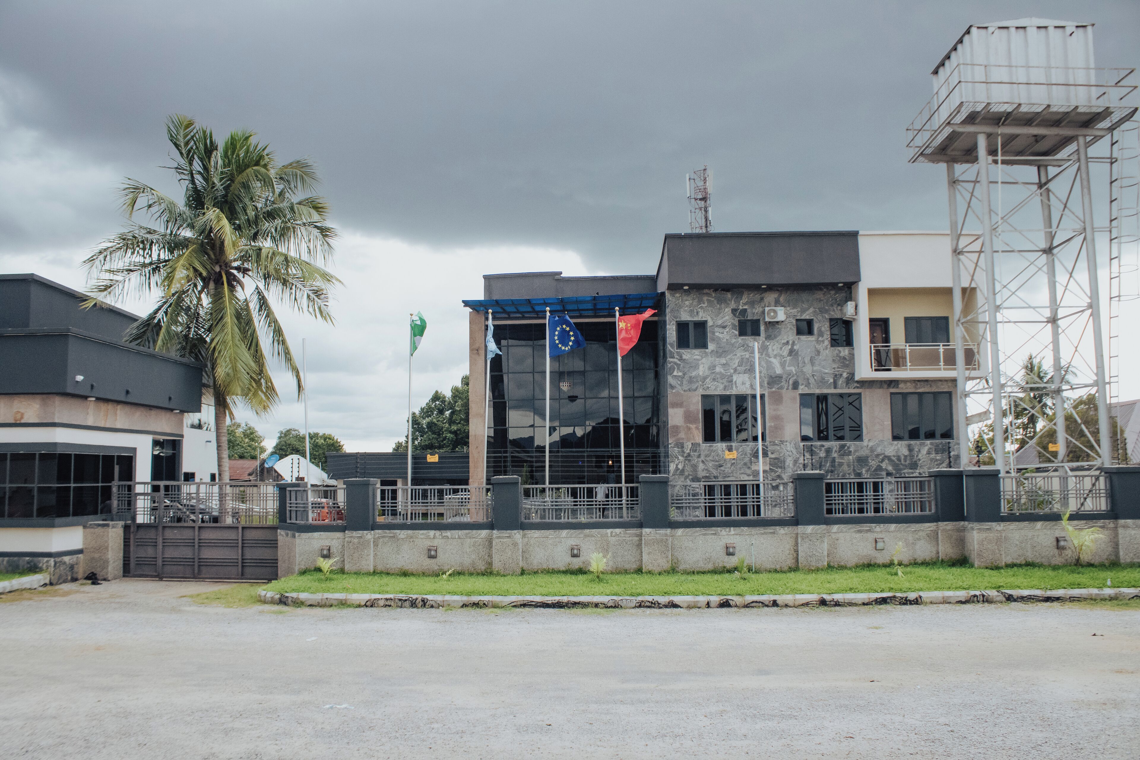A modern building with a glass facade, a palm tree, and a gated entrance.