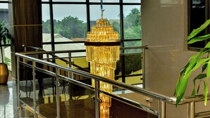 A modern interior with a glass railing, a tall, ornate chandelier, and a view of greenery outside.