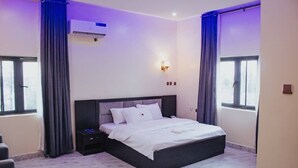 A modern bedroom with a large bed, a flat-screen TV, and a wall-mounted air conditioner.