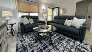 A modern living room with a dark grey sectional sofa, two side tables with lamps, a glass coffee table, and a patterned rug.