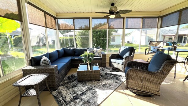 A sunroom with a sectional sofa, wicker chairs, a coffee table, and a ceiling fan.