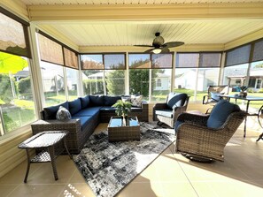 Ein Wintergarten mit Ecksofa, Korbstühlen, Couchtisch und Deckenventilator.