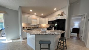 A spacious kitchen with a large island, white cabinetry, a black refrigerator, and a dining area with two stools.