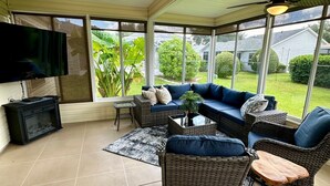 A covered patio with wicker furniture, a flat-screen TV, and a ceiling fan.