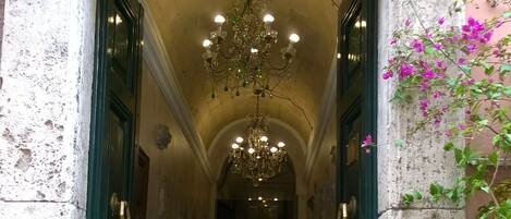 A corridor with a chandelier, green doors, and a staircase leading to an upper level.