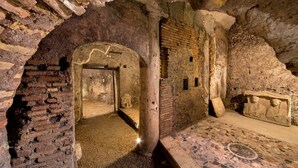 An ancient stone structure with a mosaic floor, a doorway leading to a smaller room, and a statue. - The Inn at the Roman Forum Elegant Collection - The Roman Forum Lodging. (Rome)