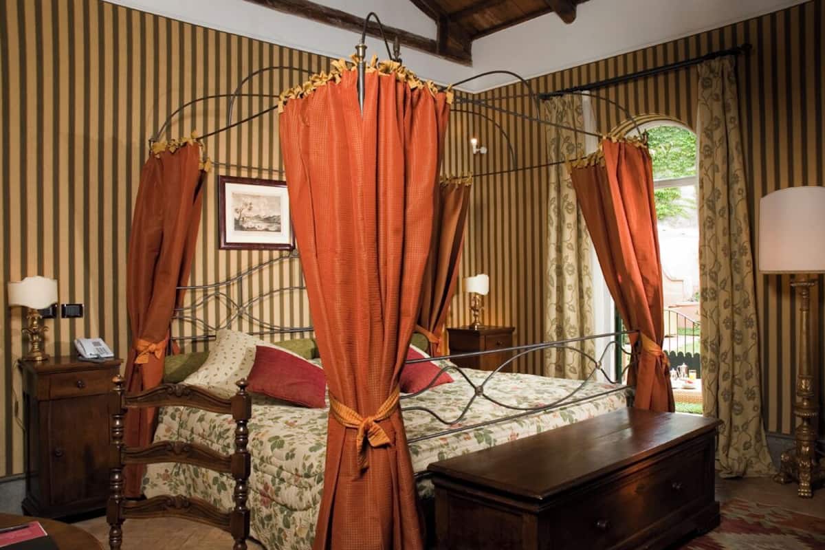 Un lit à baldaquin, une table de chevet en bois avec une lampe et une autre table de chevet également équipée d’une lampe.