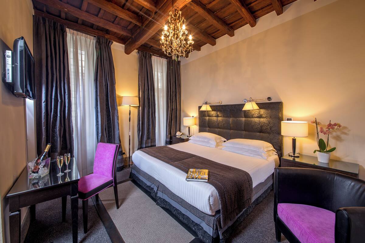 Une chambre d’hôtel avec un grand lit, un bureau avec une chaise, une télévision et un lustre.
