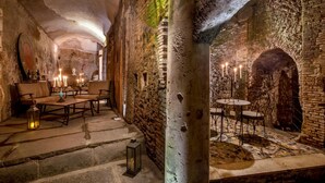 A historic interior with stone walls, a stone bench, and a table with candles. - The Inn at the Roman Forum Elegant Collection - The Roman Forum Lodging. (Rome)