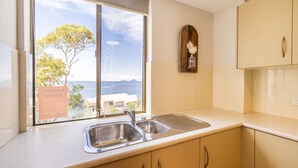 A kitchen with a double sink, wooden cabinets, and a view of the sea through a large window. - The Point 13, 5-7 Mitchell St - stunning water views, complex pool and WiFi (Soldiers Point)