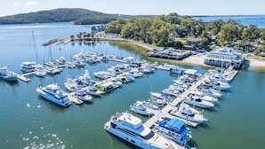A marina with numerous boats docked, surrounded by lush greenery and a hilly landscape in the background. - The Point 13, 5-7 Mitchell St - stunning water views, complex pool and WiFi (Soldiers Point)