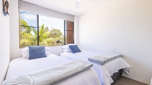 A room with two beds, a large window with a view of greenery, and a brick wall. - The Point 13, 5-7 Mitchell St - stunning water views, complex pool and WiFi (Soldiers Point)