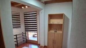 A room with a tiled floor, a wooden cabinet with shelves, a metal rack, and a door with blinds.