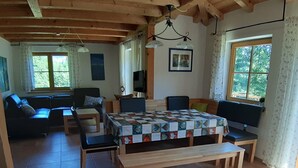 A cozy living room with a wooden table, benches, and a sofa. There are windows with curtains and a ceiling fan.