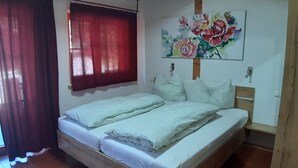 A bedroom with a wooden bed, red curtains, a floral painting on the wall, and tiled flooring.