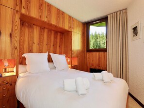 Ett hotellrum med en väggpanel av trä, en stor säng med vita sängkläder, två sänglampor och ett fönster med gardiner.