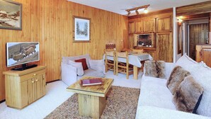 Ein gemütliches Wohnzimmer mit Holzwänden, einem Fernseher, einer Couch, einem Couchtisch und einer Essecke mit Holzkörben.