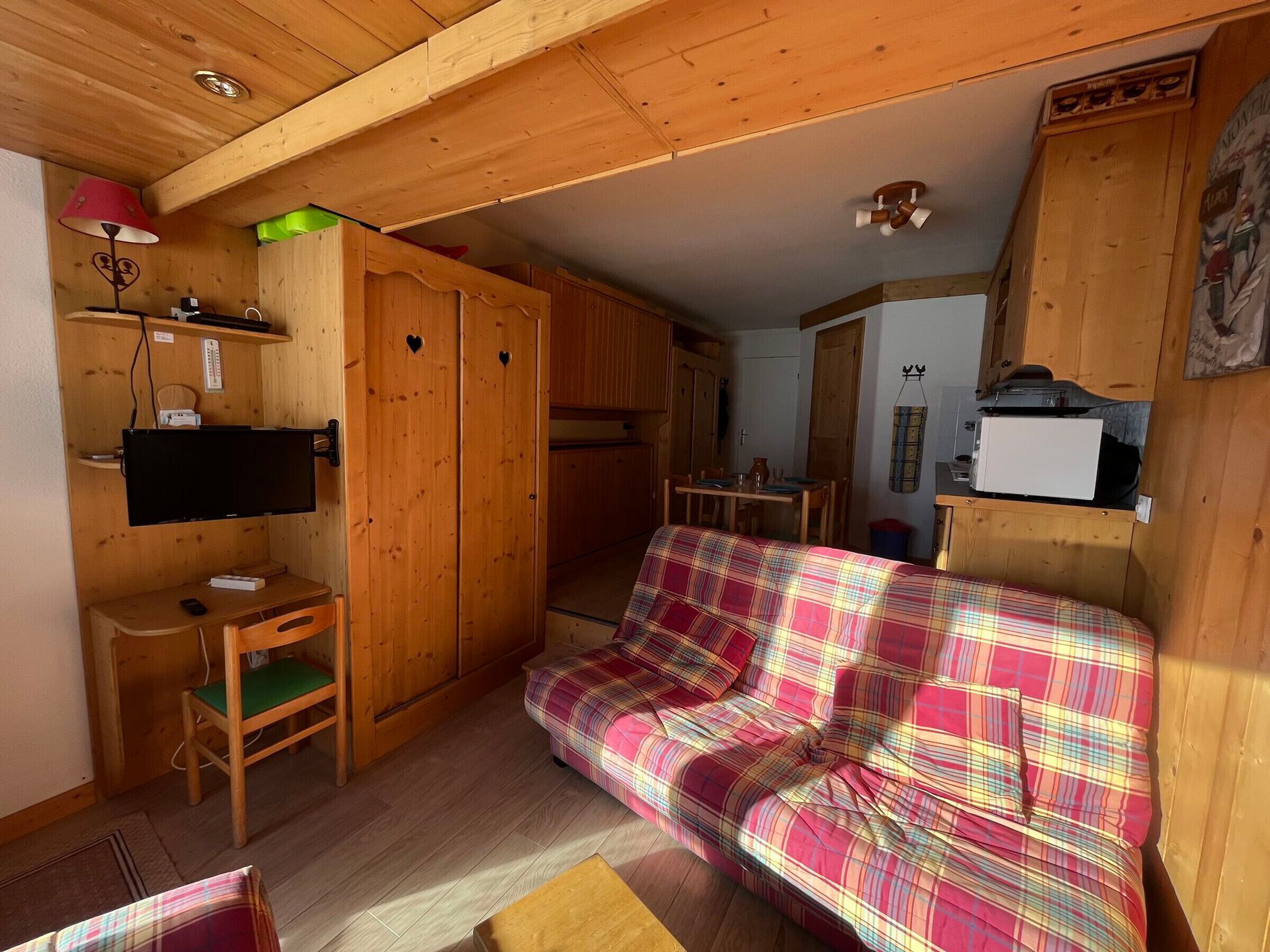 A cozy room with a plaid sofa, wooden furniture, a TV, and a microwave.