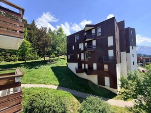 A modern multi-story building with balconies, surrounded by greenery and a clear sky.