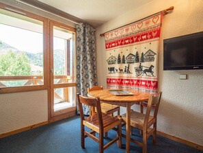 Una mesa de madera con cuatro sillas, un ventanal con vistas a un paisaje montañoso y un tapiz con escenas campestres en la pared.