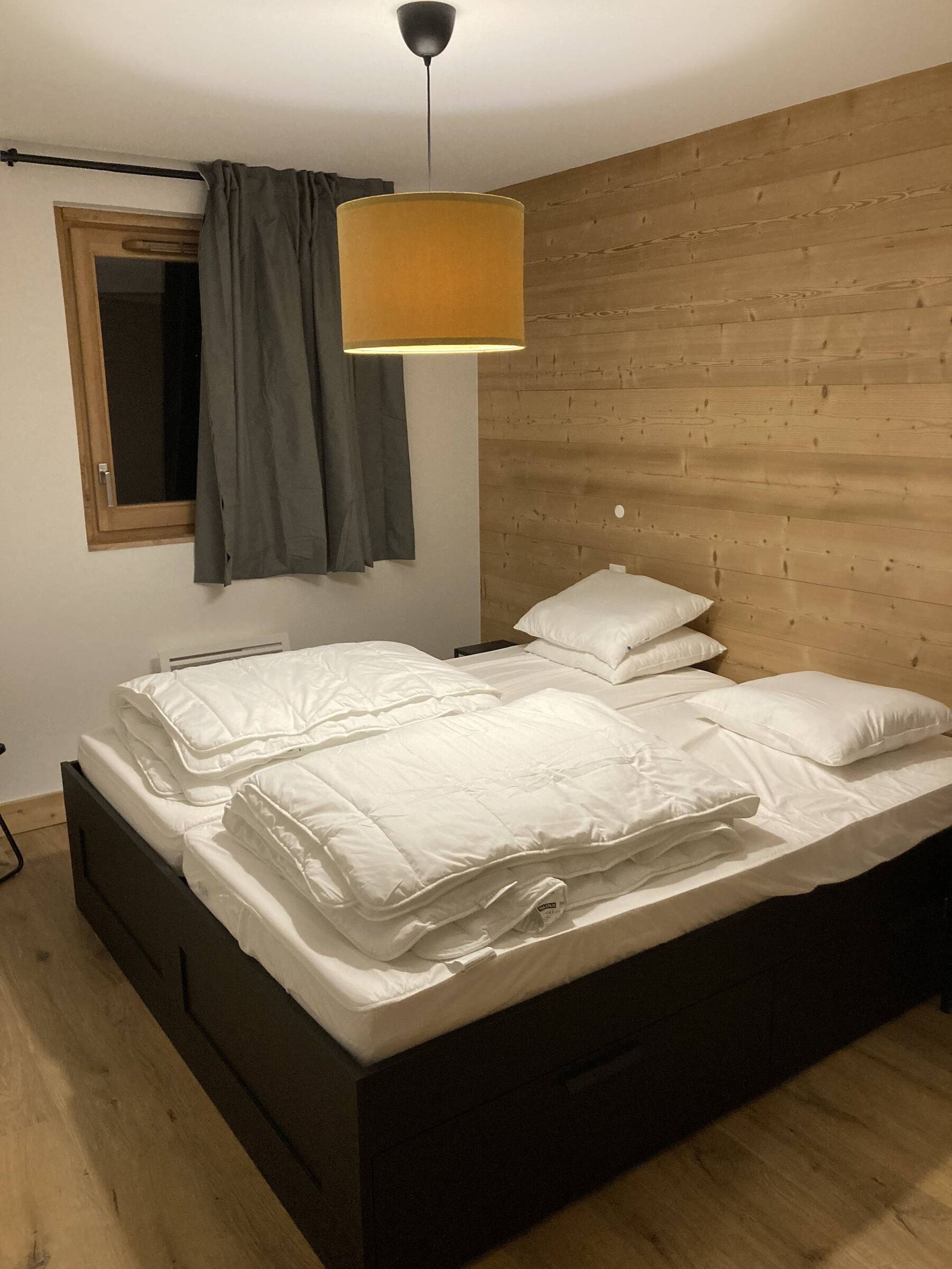 Ein Schlafzimmer mit hölzernem Kopfteil, einem Bett mit weißer Bettwäsche, einer Hängelampe und einem Fenster mit Vorhängen.