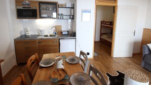 A compact kitchen with wooden cabinets, a microwave, and a sink. There is a dining table set with plates and glasses. A bunk bed is visible in the adjacent room.