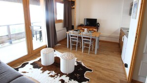 A cozy room with a wooden floor, a sofa, a dining table with chairs, a television, and a cowhide rug.