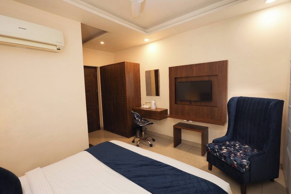 A hotel room with a bed, a desk with a chair, a TV mounted on the wall, and a wardrobe.