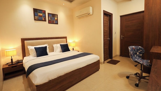 A hotel room with a large bed, bedside lamps, an air conditioning unit, a desk with a chair, and a door. - Hotel RK Grande (Ludhiana)