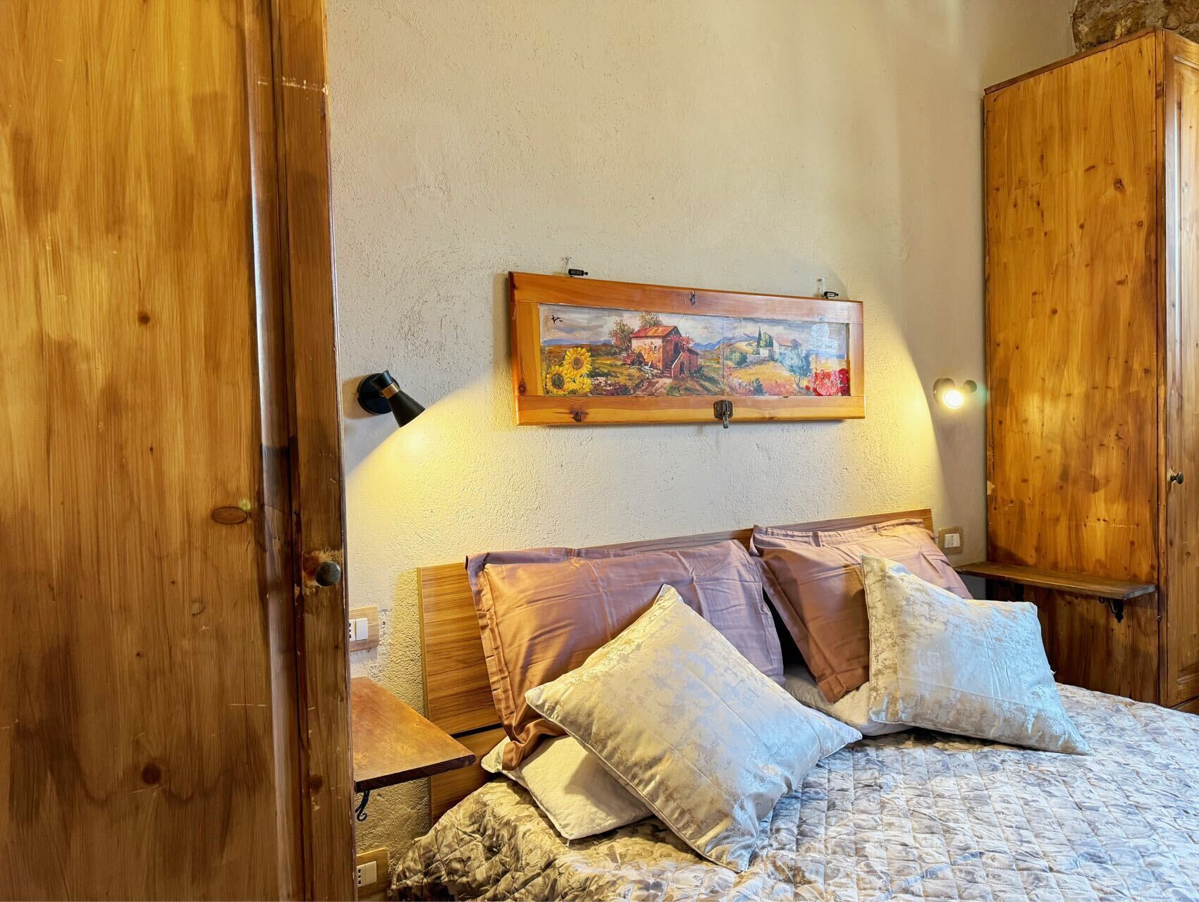 A bedroom with a wooden bed, a painting on the wall, and a wooden wardrobe.