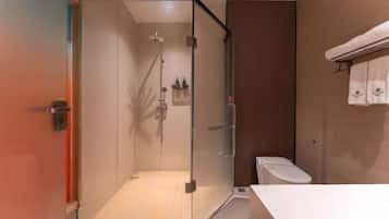 Un baño moderno con ducha envuelta en vidrio, un inodoro blanco y un perchero con toallas.