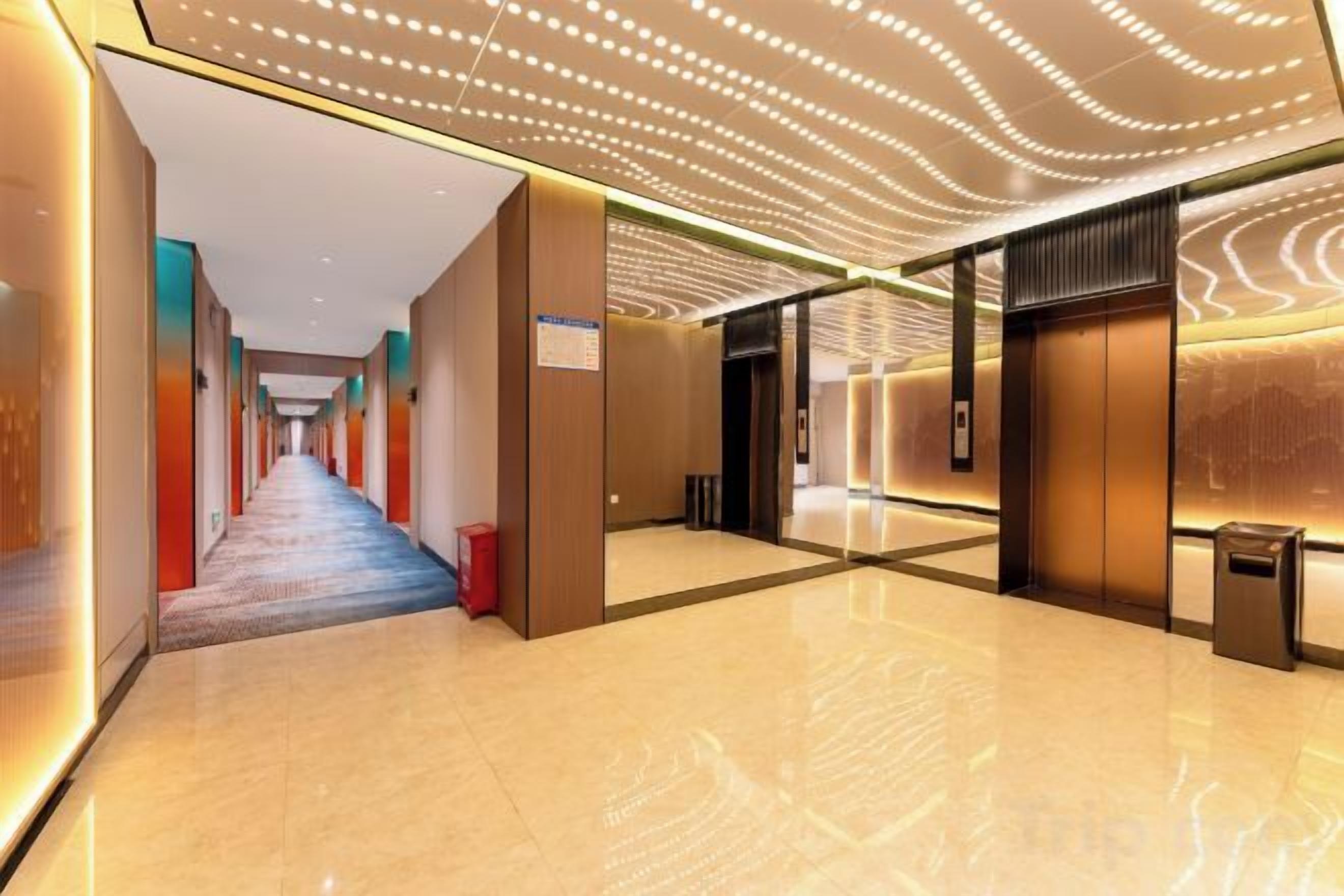 Un corridoio moderno di un hotel con un lungo disimpegno, una zona reception e un ascensore ben visibile.