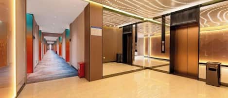 A modern hotel corridor with a long hallway, a reception area, and a visible elevator.